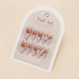 Detail of brown gradient press-on nails with white French tips, bows and pearls