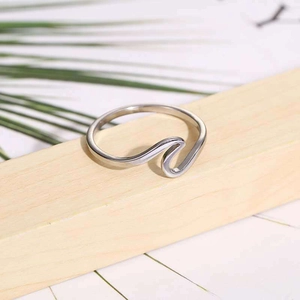 Macro shot of silver wavy stainless steel ring placed on a minimalist wood surface