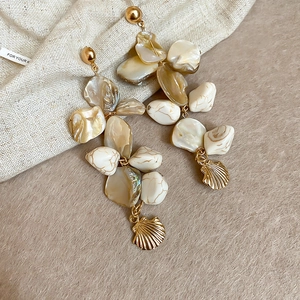 Detail of long drop earrings with irregular cream shell beads and golden shell charms