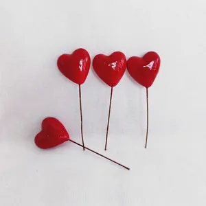 Close-up of four glossy red heart-shaped cake toppers with brown stems for DIY decor