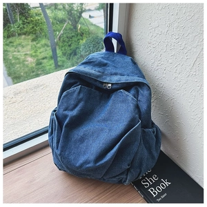 Close-up of blue denim backpack with top handle on a wooden table by the window