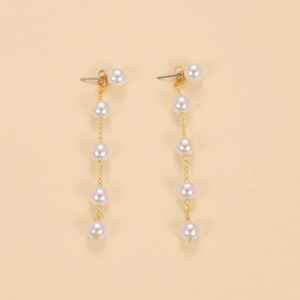 Detail of long gold chain tassel earrings featuring five glossy pearls in a tiered design