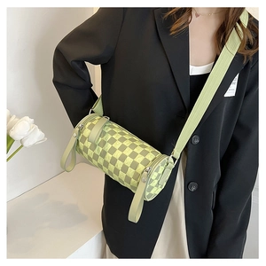 Detail view of a green checkerboard cylinder bag with wide canvas strap on model