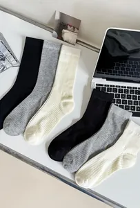 Three pairs of ribbed combed cotton socks in black, grey, and white on a clean desk