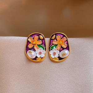 Macro detail of vintage enamel earrings with pearl accents and 3D floral oil painting motifs