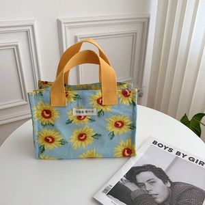Detail of sunflower printed lunch tote bag with yellow woven handles on a white table