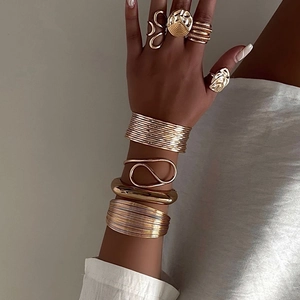 Detail von geschichteten Goldarmbändern und breiten Armreifen kombiniert mit Ringen am Handgelenk