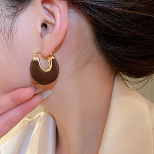 Macro shot of U-shaped gold earrings with brown velvet flocking on ear lobe