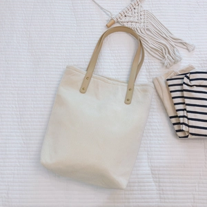 Minimalist cream corduroy tote bag with brown leather handles on a quilted white fabric