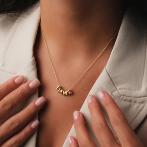 Close-up of golden necklace with EMMA letter beads worn by a model in a beige suit