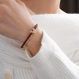 Close-up of gold double-layer bracelet with burgundy cord and pavé zircon X-link detail