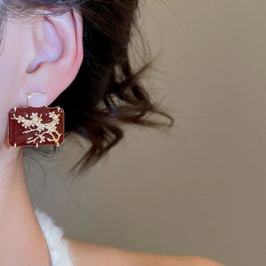 Detail of red enamel square stud earring with gold plum blossom branch on ear