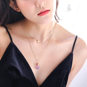 Detail of layered gold necklace featuring a purple hexagonal crystal pendant on a model