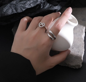 Detail of S925 sterling silver knotted heart ring and minimalist wide band on fingers