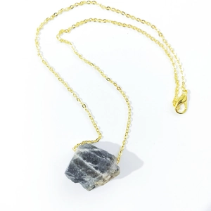 Detailed shot of irregular natural raw crystal pendant with fine golden chain necklace