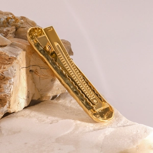 Strukturierte Haarspange aus goldfarbenem Metall mit Hammerschlag-Optik auf Naturstein