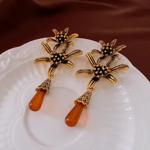 Vintage gold flower earrings with amber teardrop pendants on a white embossed ceramic plate