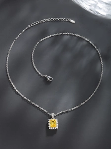 Detail of silver chain with square yellow gemstone pendant and white zircon halo