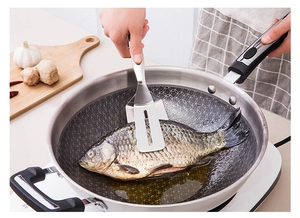Close-up of stainless steel fish spatula lifting a fish from a frying pan in a kitchen