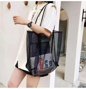 Close-up of a large black mesh tote bag with durable shoulder straps worn by a model