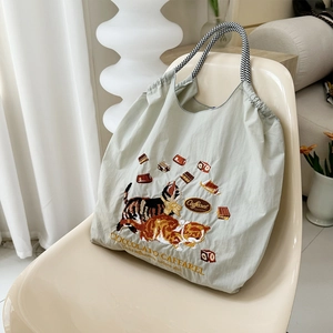 Detail of cat embroidery and striped handles on light green nylon tote bag on a chair