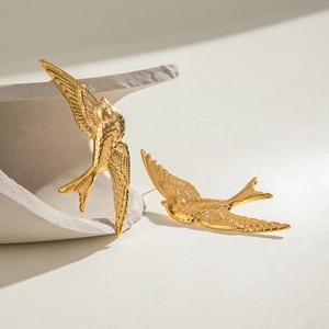 Vintage golden stainless steel swallow stud earrings on a textured minimalist background