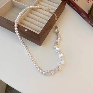 Close-up of baroque pearl necklace with gold clasp laid on a white surface and book