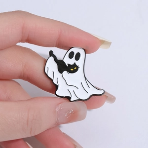 Hand holding a cute Halloween ghost enamel pin with a black cat on grey backdrop