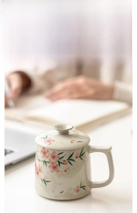 Detail of 350ml hand-painted peach blossom ceramic office mug with lid on a desk