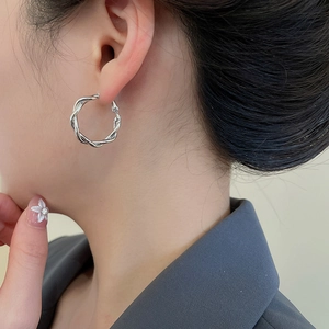 Close-up of elegant silver twisted hoop earrings worn by a model in a grey suit