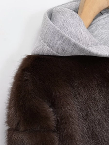 Detail einer braunen Pelzimitat-Jacke mit grauer Baumwollkapuze am Holzbügel
