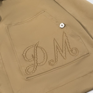 Detail of khaki jacket with DM 3D embroidery, premium fabric texture and button closure