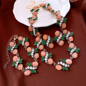 Detail of vintage gold necklace and bracelet set with pink oval resin and green leaf gems