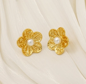Macro shot of gold floral earrings with textured petals and center white pearl detail