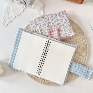 Detail of floral zipper pouch and blue plaid notebook with spiral binding on a straw mat