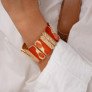 Macro detail of geometric gold bracelet with orange enamel sections and hammered texture