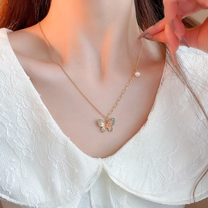 Detail of gold butterfly necklace with pink-green enamel and pearl on lace collar