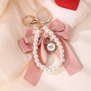 Detail of pink bow and pearl heart keychain on beige silk background with golden metal hardware