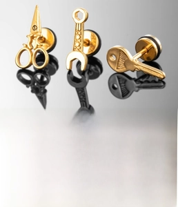 Détail macro de boucles d'oreilles en acier doré en forme de clé, ciseaux et clé à molette