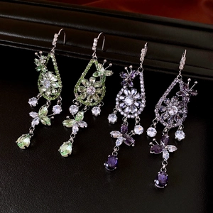 Detail of luxury zircon teardrop earrings in green and purple on a dark leather texture