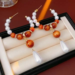 Detail of drop earrings with orange swirl beads and teardrop pearls on velvet lining
