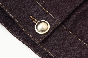 Détail de la veste en jean foncée avec coutures jaunes contrastées et boutons en métal argenté
