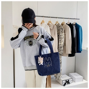 Detail of dark blue corduroy tote bag with bunny embroidery and cute cow plush charm