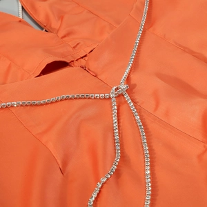 Détail d'une combinaison en satin orange avec nœud décoratif et chaîne en strass brillant