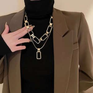 Detail of layered gold link chain and rectangular pendant on woman's neck