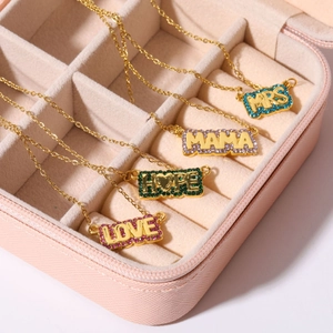 Close-up of gold necklaces with MRS, MAMA, HOPE, LOVE pendants in a pink jewelry box