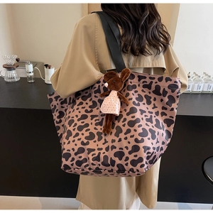 Detailed side view of leopard print tote bag with brown plush bunny charm and wide strap