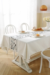 Detailed view of floral embroidery and fringe edge on a beige linen-textured tablecloth