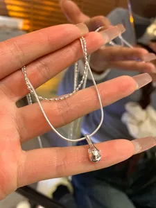 Detail of a double-layered stainless steel necklace featuring a polished water drop pendant