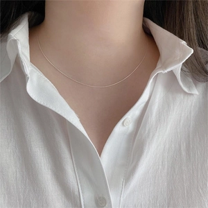 Close-up of minimalist sterling silver chain necklace worn on collarbone with white shirt